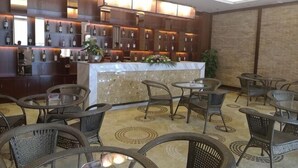 Uma área de bar com várias opções de assento, incluindo mesas redondas e cadeiras de vime, e um balcão com bancada de mármore branco.