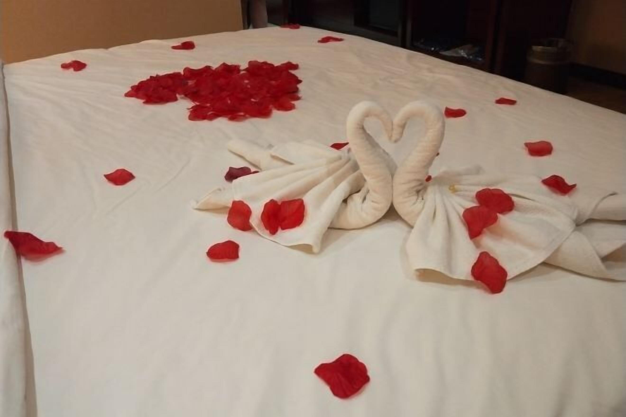 A bed with rose petals and a swan towel arrangement.