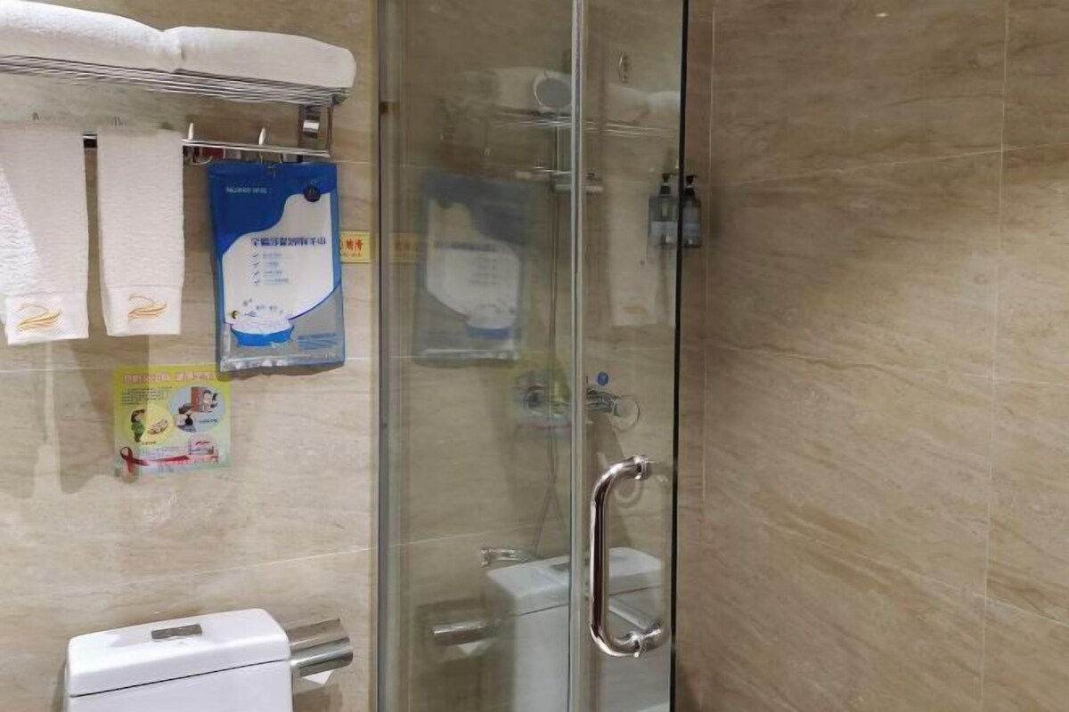 A bathroom with a glass shower enclosure, a toilet, a hand dryer, and a towel rack with towels.