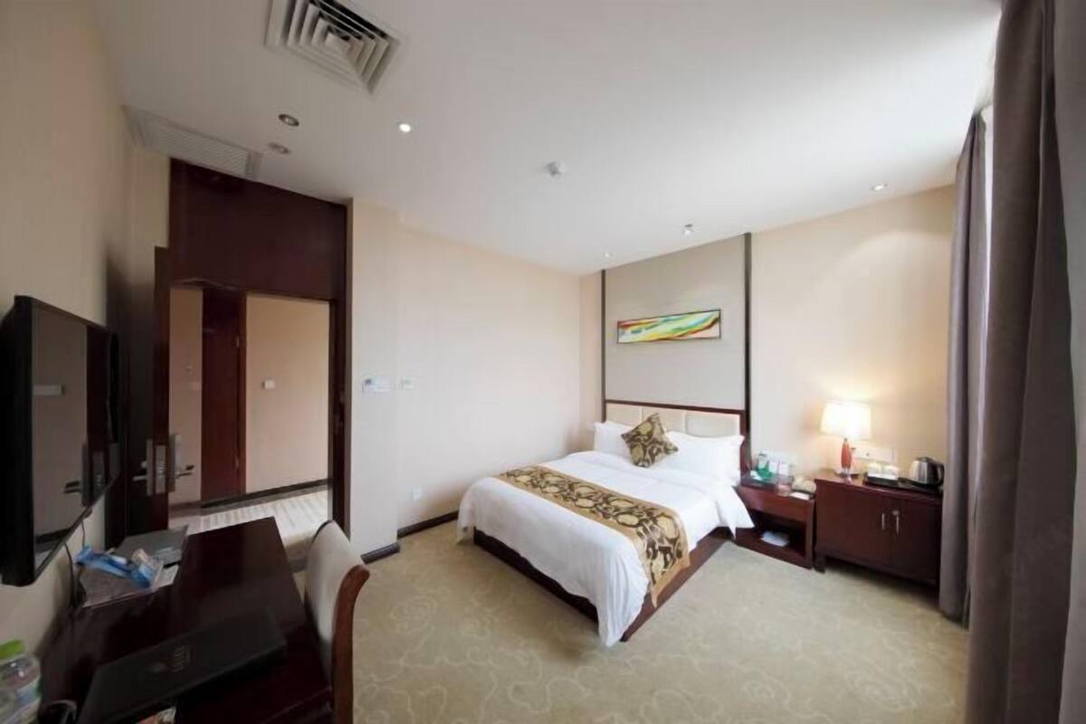 A hotel room with a bed, bedside table, lamp, and a TV.