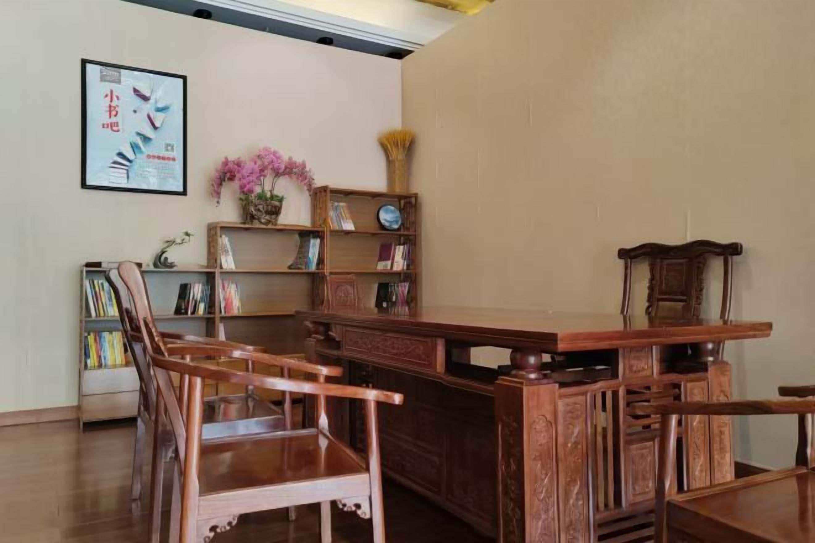 A traditional wooden desk with chairs, a bookshelf, and a framed picture on the wall.