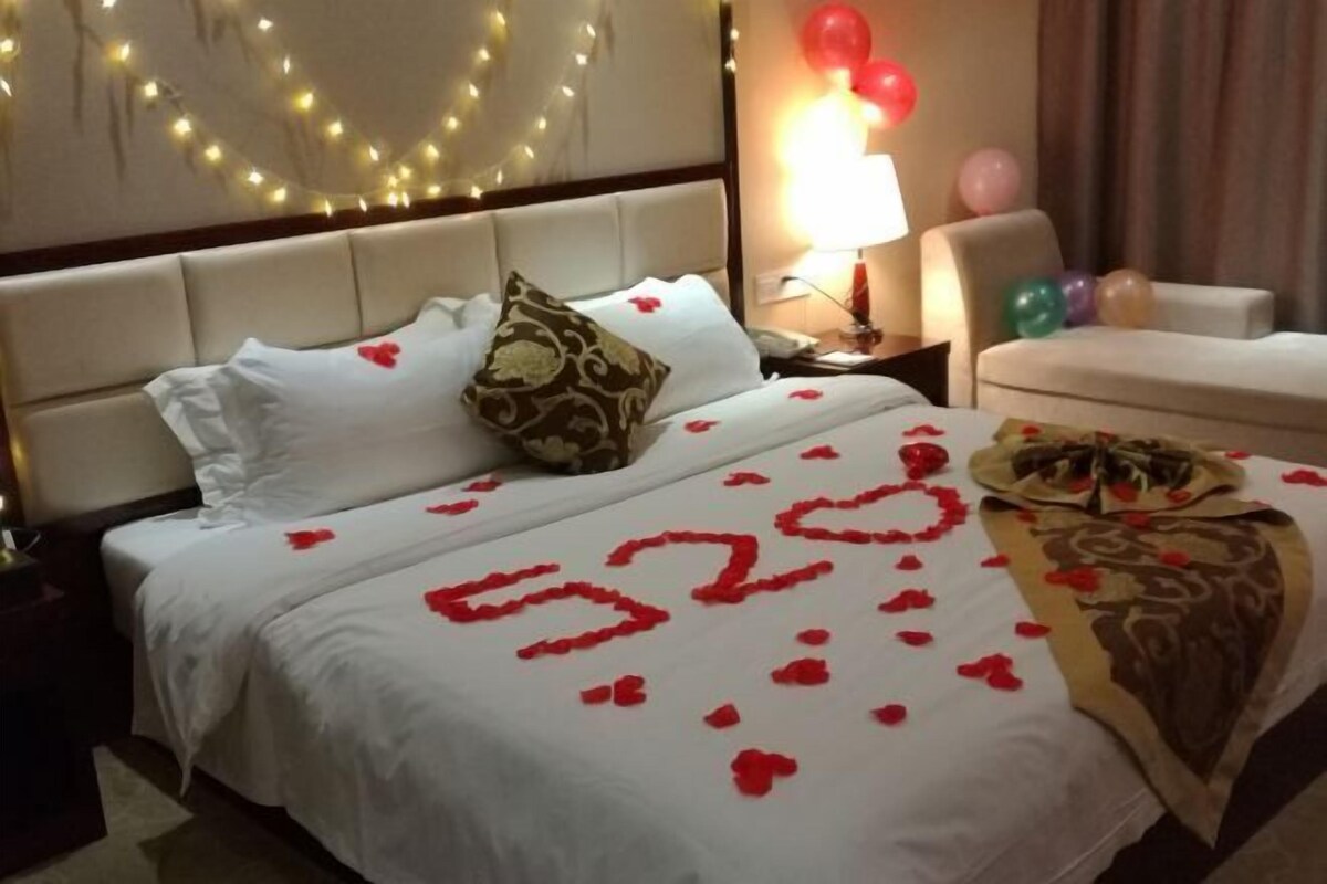 A hotel room with a bed adorned with rose petals and a heart-shaped number '520'.