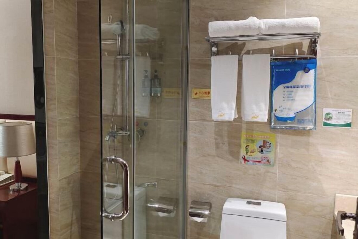 A bathroom with a glass shower enclosure, a towel rack with towels, a toilet, and a hand dryer.