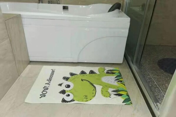 Une salle de bain avec une baignoire blanche, un espace douche et un tapis vert à motifs de dinosaures sur le sol.