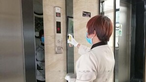 Uma pessoa com jaqueta branca usando um painel de controle de elevador digital, com visor mostrando o número 5.