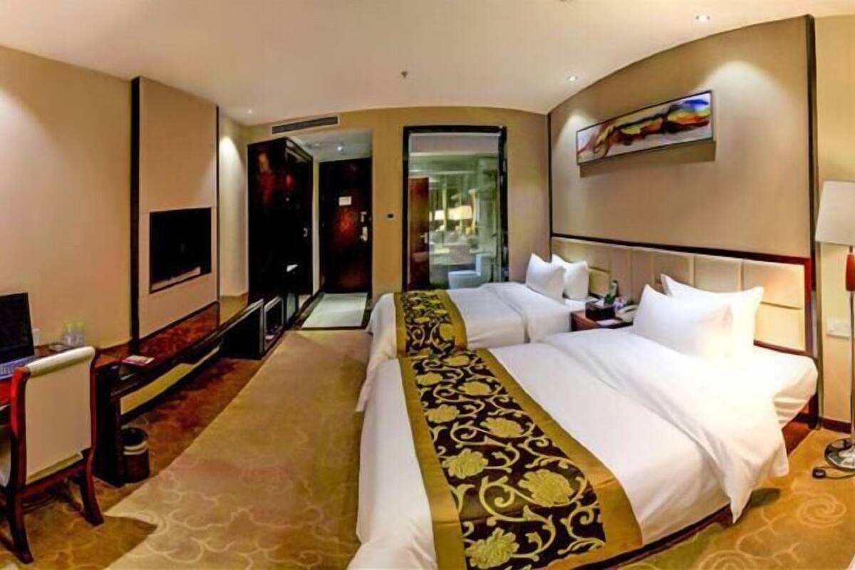 A hotel room with a large bed, a desk, a TV, and a painting on the wall.
