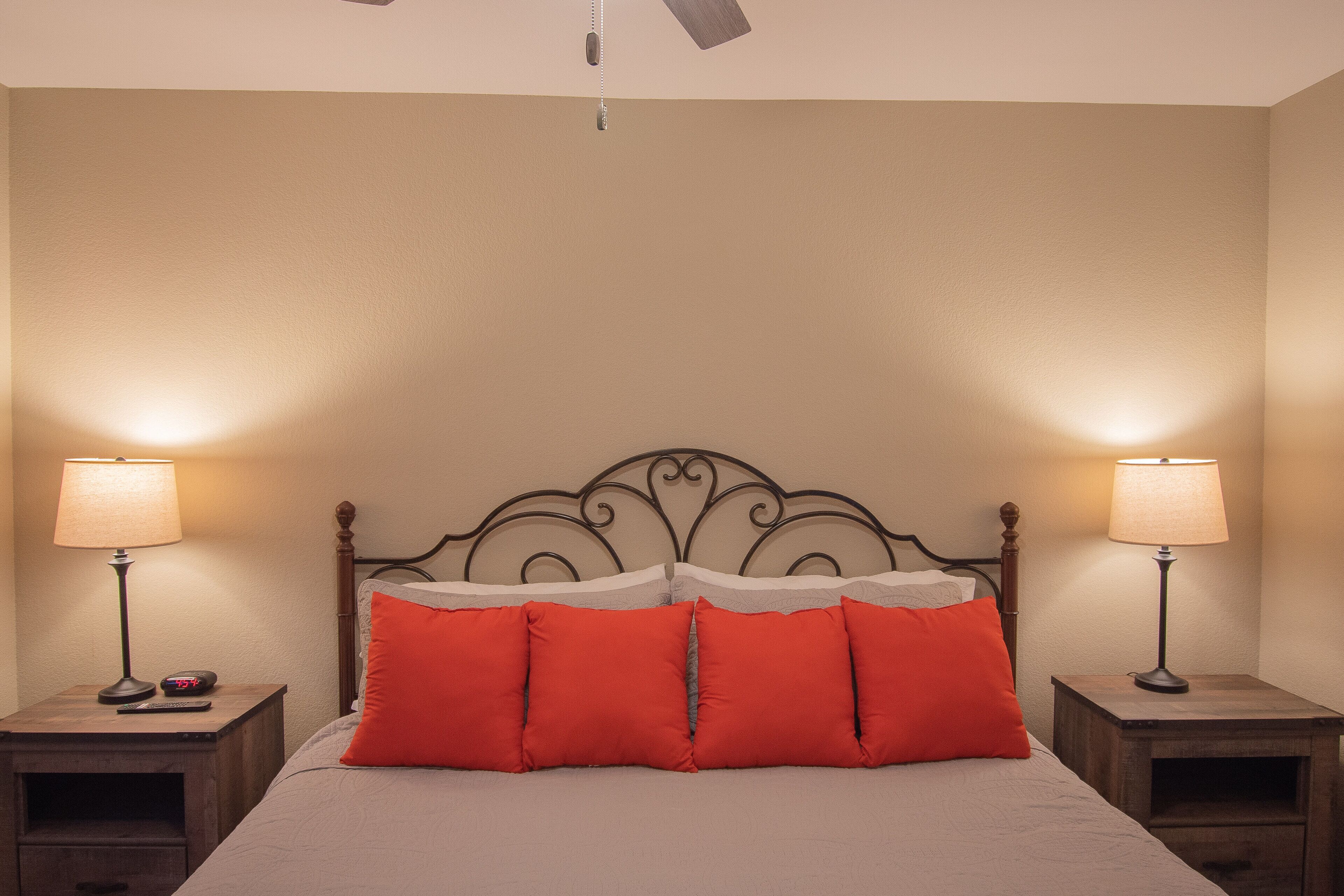 A neatly made bed with red pillows, two bedside tables with lamps, and a wooden headboard.