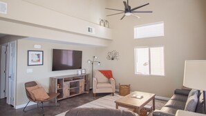 Amplia sala de estar con televisor de pantalla plana, ventilador de techo, sofá, sillón y mesa de centro.