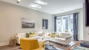 Un salon moderne avec un ensemble de canapés blancs, un fauteuil jaune, une table basse et une grande fenêtre avec des rideaux.