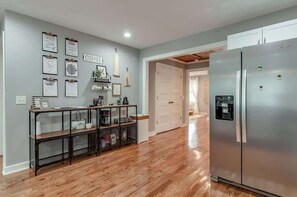 Eine Küche mit Edelstahl-Kühlschrank, Holzboden und einem Metall-Konsolentisch mit diversen Küchenutensilien.