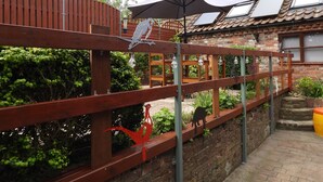 A wooden fence with decorative metal cutouts, a brick wall, and a tiled roof building in the background. - Eric House (Filey)