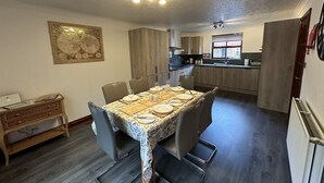 A dining area with a table set for six, a kitchen in the background, and a ceiling with a decorative pattern. - Eric House (Filey)