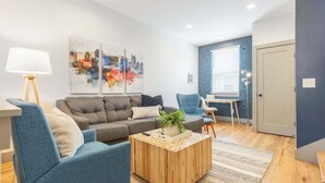A modern living room with a grey sofa, blue armchairs, a wooden coffee table, and a cityscape artwork on the wall.