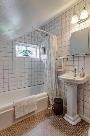 A bathroom with a bathtub, a sink, a window, and a mirror.