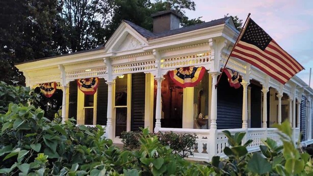 A two-story house with a porch, columns, and an American flag. - Market Street House - Enchanted Victorian (Nashville)