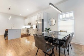A modern kitchen with white cabinets, a central island, and a dining area with a glass table and black chairs.