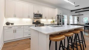 Una cocina moderna con armarios blancos, electrodomésticos de acero inoxidable y una isla central con taburetes de bar.