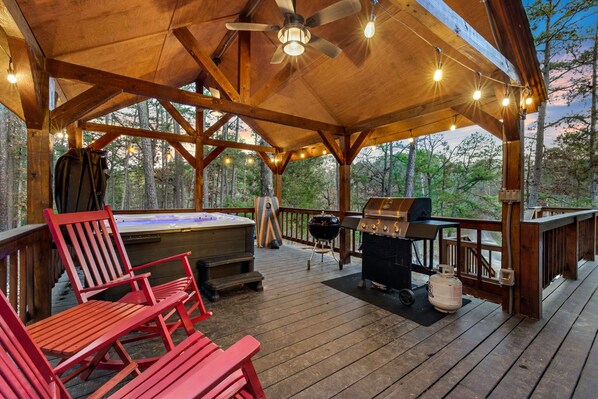En overdækket terrasse med boblebad, grill og røde Adirondack-stole.