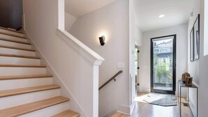 A modern staircase with wooden steps and white railings leading to a bright hallway with a glass door and a view of greenery outside. - The Bel- Vandy (Nashville)