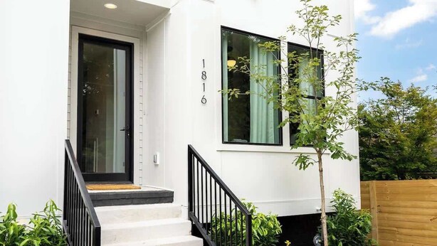 Une maison moderne à deux étages, avec une façade blanche, une porte noire et un petit escalier menant à l’entrée.