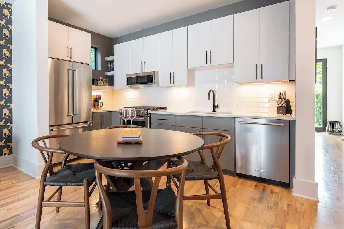 A modern kitchen with white cabinets, stainless steel appliances, and a round dining table with chairs.