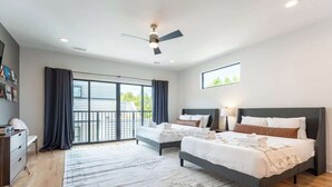 Une chambre moderne avec deux lits, un ventilateur de plafond et une grande fenêtre avec des rideaux.