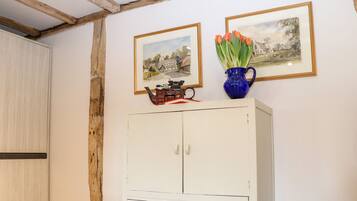 A room with a white cabinet, wooden beams on the ceiling, and two framed paintings above it.
