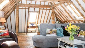 An attic room with a sloped wooden ceiling, a grey sofa, a small table, and a lamp.