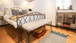 A bedroom with a bed, a bench, a window with a view, a wall-mounted shelf, and a bedside table.