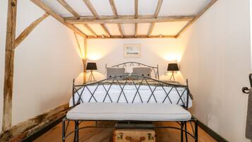 Um quarto pequeno e rústico, com estrutura de cama em metal, duas luminárias de apoio e teto de madeira.
