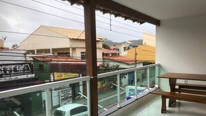 A balcony with a view of a street, a car, and a building with a sign. - Pousada Central de Arraial (Arraial do Cabo)
