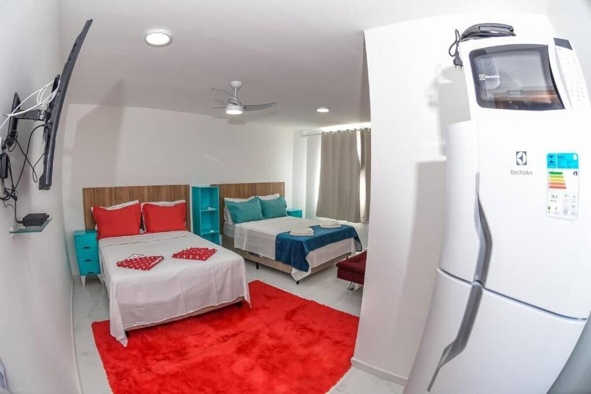 Een hotelkamer met twee bedden, een rood tapijt, een witte koelkast en een plafondventilator.