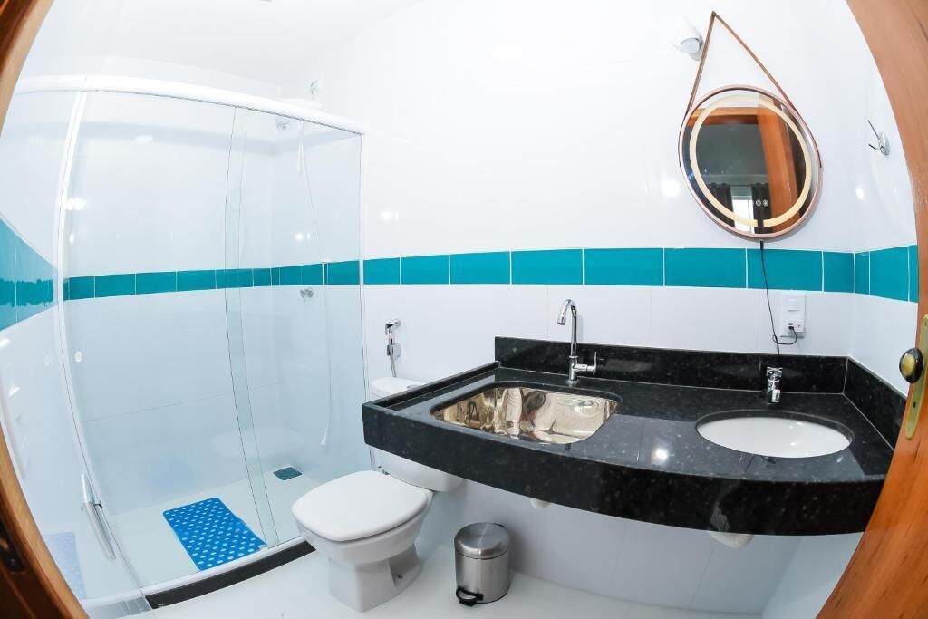 Un baño con cabina de ducha de vidrio, inodoro blanco, lavabo negro con espejo y un cubo de basura.