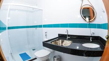 A bathroom with a glass shower enclosure, a white toilet, a black sink with a mirror above it, and a trash bin.