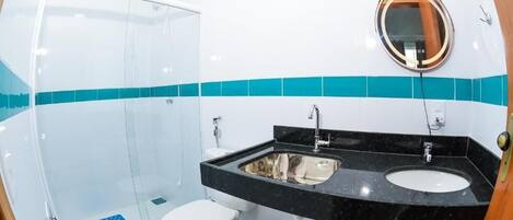 Un baño con cabina de ducha de vidrio, inodoro blanco, lavabo negro con espejo y un cubo de basura.