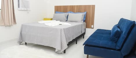 Un dormitorio con una cama, un sofá azul, un manto blanco y mullido, y un calentador fijado a la pared.
