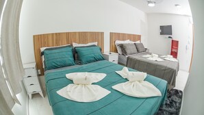 A modern hotel room with a large bed, a smaller bed, a TV, a desk, and a red cabinet. - Pousada Central de Arraial (Arraial do Cabo)