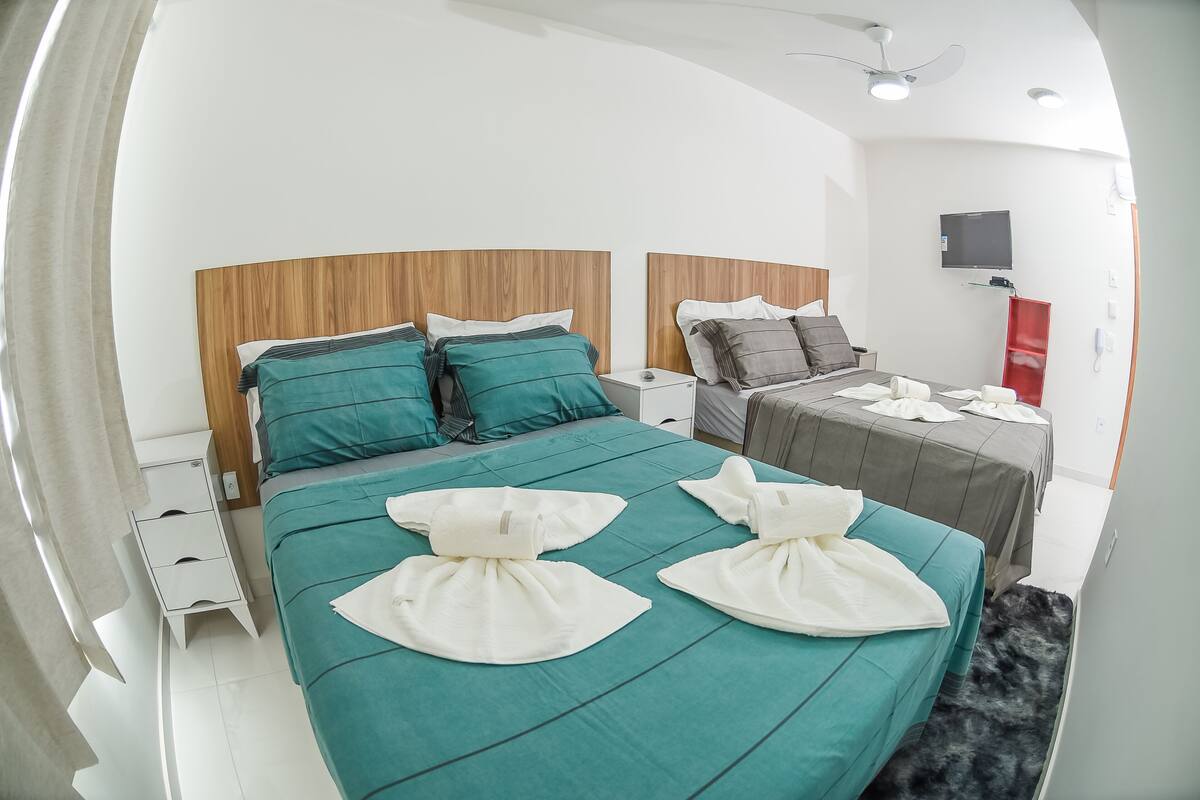 Een moderne hotelkamer met een groot bed, een kleiner bed, een televisie, een bureau en een rode kast.