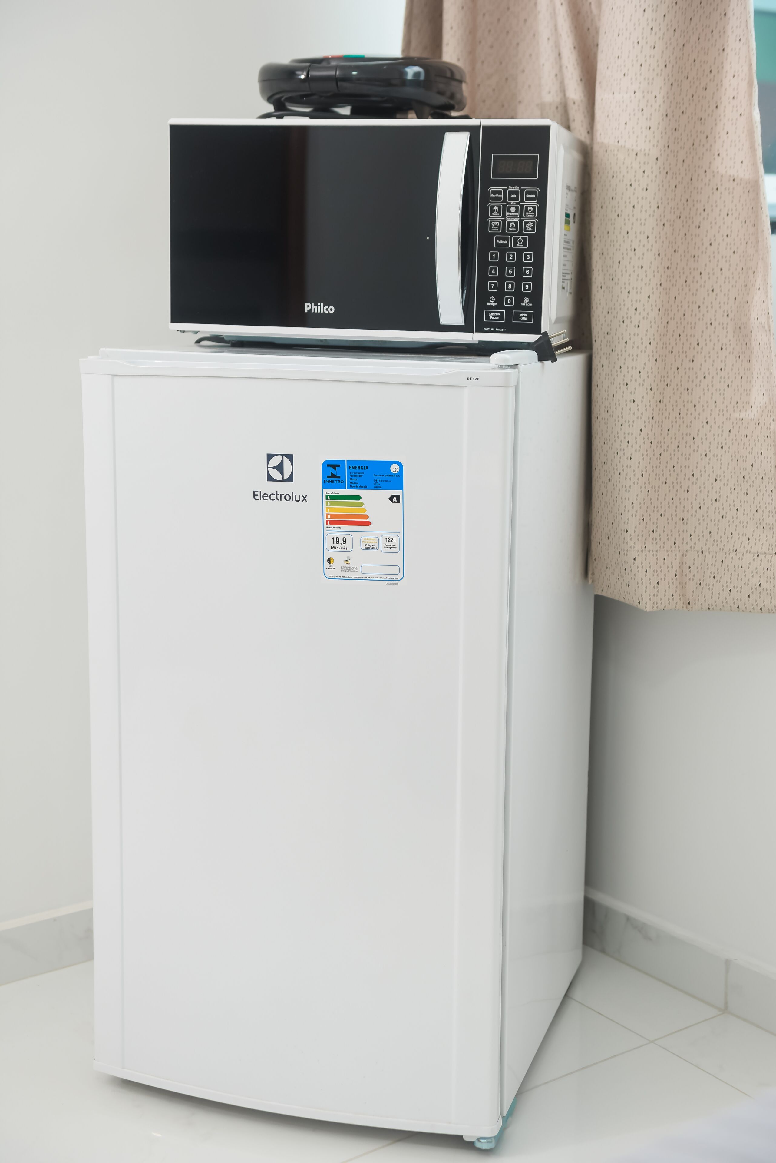 Ein kompakter Kühlschrank mit digitaler Anzeige und einer Mikrowelle darüber.