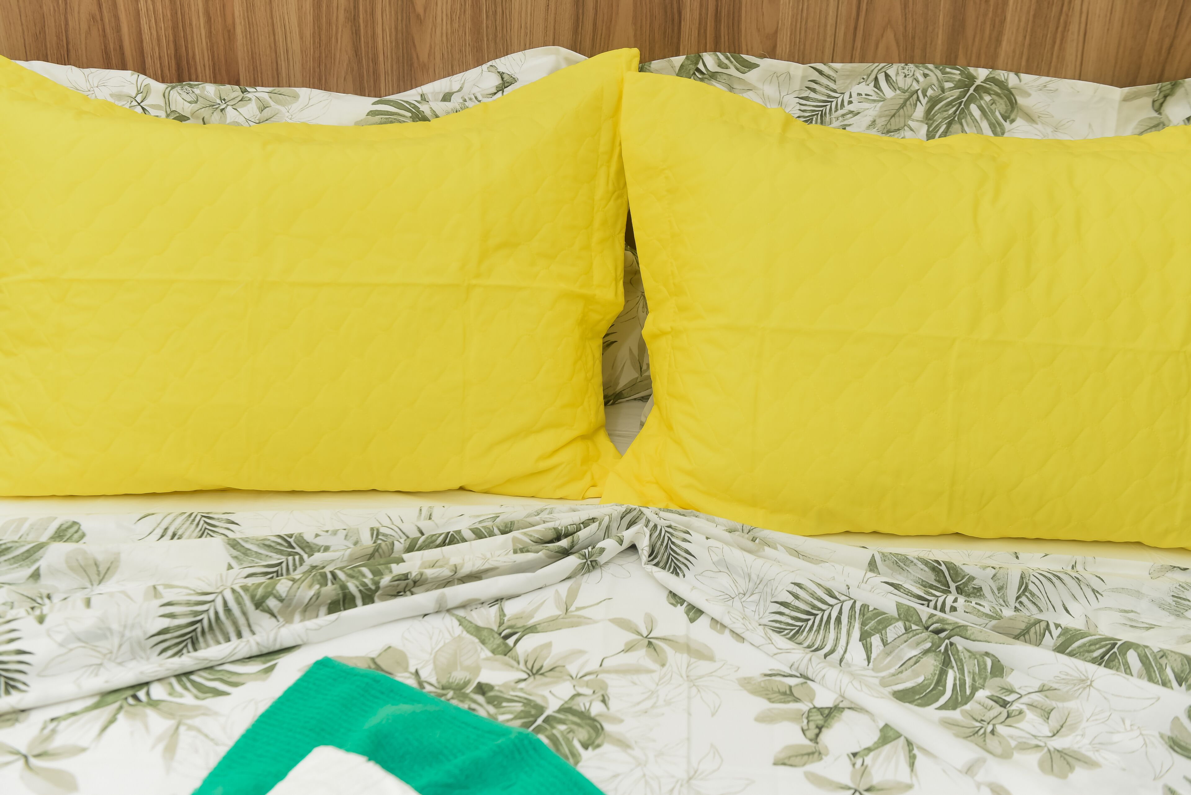 A bed with a floral-patterned bedspread and two bright yellow pillows.