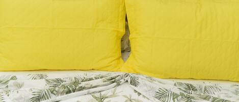 Una cama con una colcha de estampado floral y dos almohadas amarillo brillante.