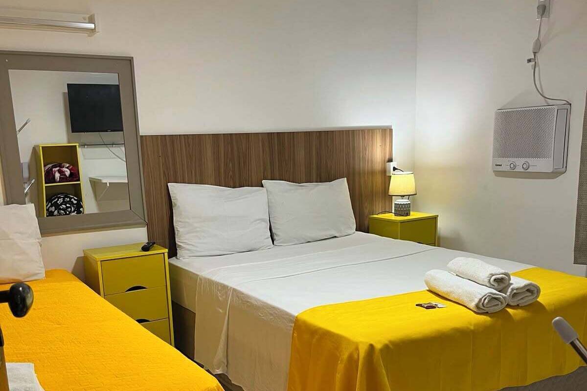 Een hotelkamer met twee bedden, een nachtkastje met een lamp, een televisie en een wandairconditioner.