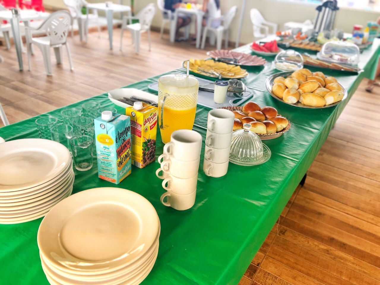 A breakfast buffet with plates, cups, and various food items on a green table.