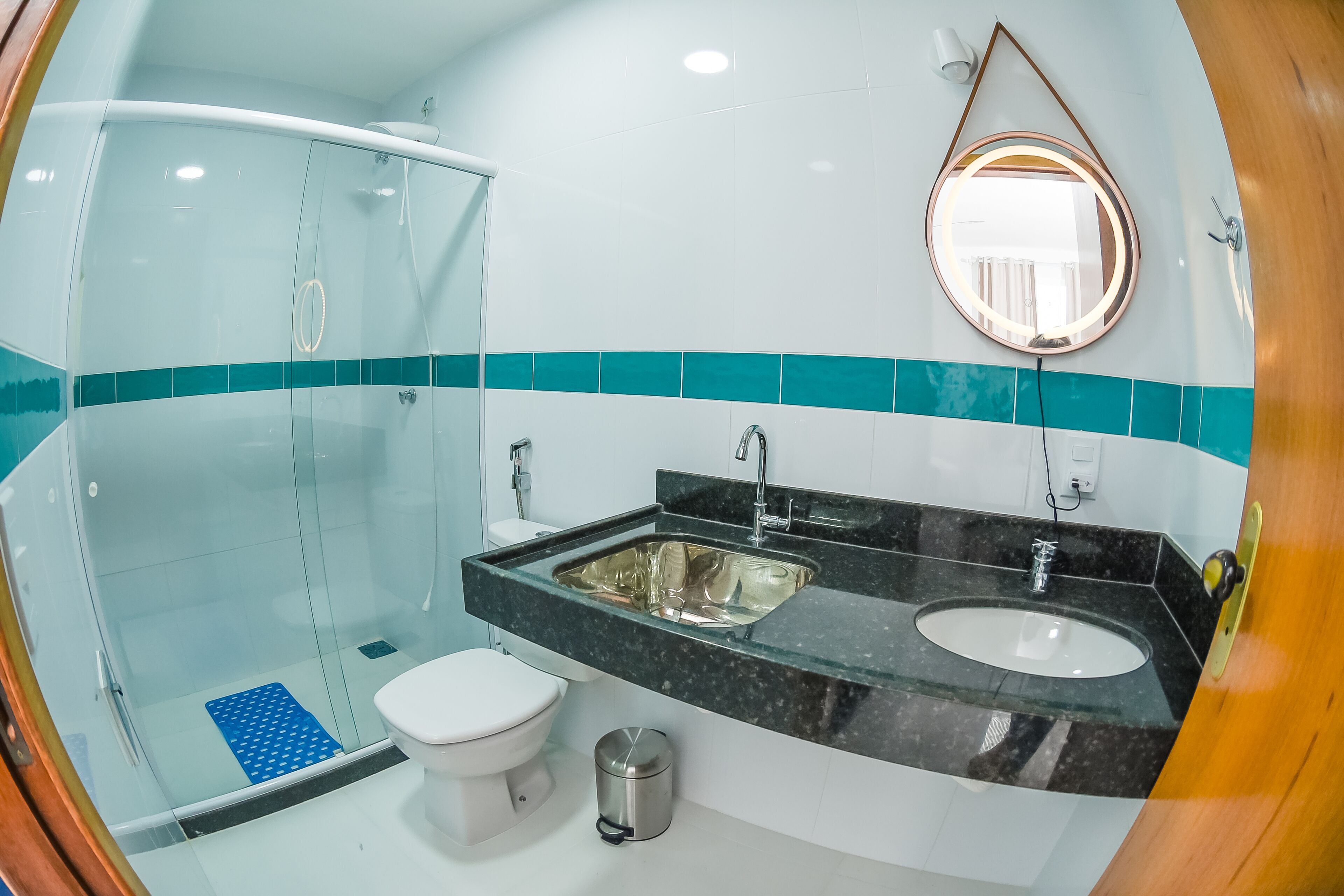 Une salle de bain moderne avec une douche à parois de verre, des toilettes blanches, un lavabo avec un miroir et des touches de couleur turquoise sur les murs.