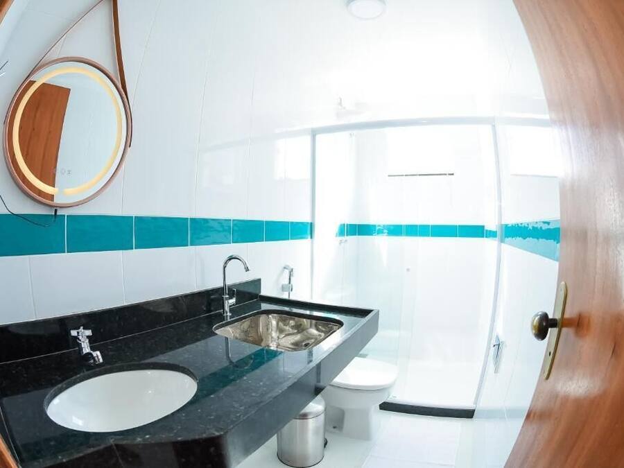 Un baño con lavamanos negro, espejo y retrete blanco.