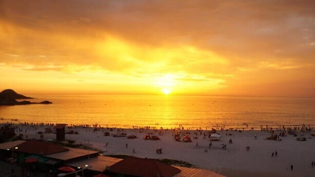 A beach with a sunset, people, and beach umbrellas. - Pousada Central de Arraial (Arraial do Cabo)