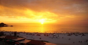 Una playa con un atardecer, gente y sombrillas.