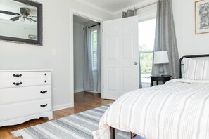 A bedroom with a bed, a dresser, a ceiling fan, a door leading to a balcony, and a window with curtains.