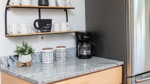 Una cuina amb armaris de fusta, un frigorífic d'acer inoxidable, una cafetera i diverses tasses sobre una prestatgeria.