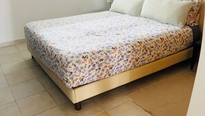 Une chambre à coucher avec un lit, une fenêtre avec des stores, une table de chevet et un miroir.